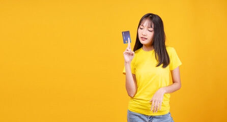 Thoughtful young Asian woman looking at blue credit card, considering shopping purchase or checking...