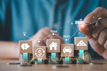 Wooden blocks with finance icons placed on stacked coins showing a rising graph from 2022 to 2026...