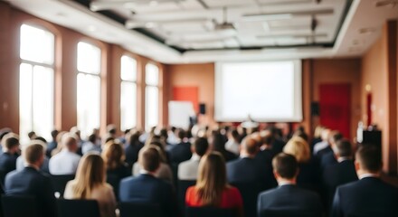 Fototapeta premium Audience attending a business conference or seminar in a large room with a presentation screen in the background, view from behind