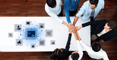 A group of professionals gathers around a table, placing their hands together in unity, with...