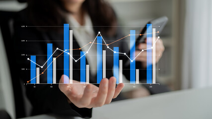 A businesswoman analyzes digital financial graphs while holding a smartphone in a modern office. Focus on growth and success using data insights in professional environment. Scalp