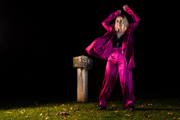 Waacking dancer in fuchsia outfit posing on grass at night