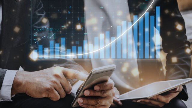 Modern workspace image featuring hands holding a smartphone and tablet with financial charts and graphs, depicting data analysis and growth strategies in business. Copula - Powered by Adobe