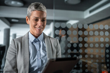 Businesswoman standing in office using digital tablet smiling