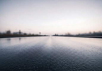 Endless stretch of wet highway at dusk with distant cityscape view