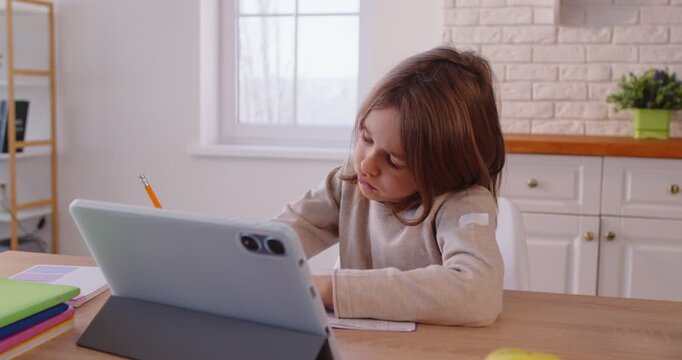 Portrait of upset little child boy tired from doing school homework sitting at the desk at home. Kid studying online class on a tablet during remote lesson.. Education and knowledge. 4k video.