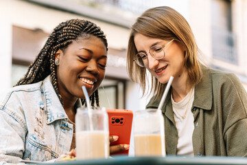 Diverse friends laughing and sharing smartphone content at cafe