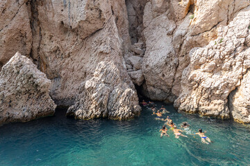 People swim on a beautiful beach in the Adriatic Sea among huge rocks in clear sea water. Caves in...