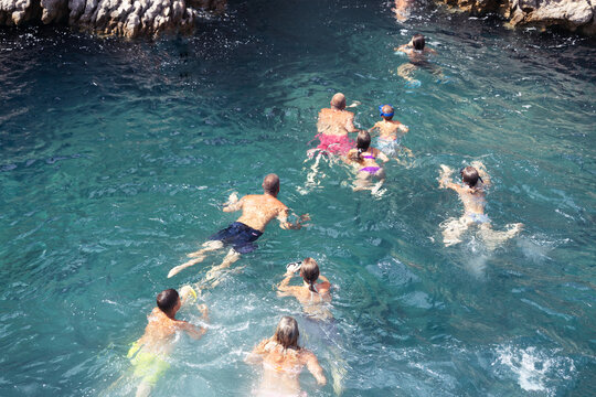 People swim on a beautiful beach in the Adriatic Sea among huge rocks in clear sea water. Caves in the rocks on the sea