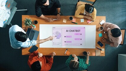 A diverse team collaborates on developing an AI chatbot in a modern office space, engaging in discussion and brainstorming innovative ideas while using digital technology. Raster