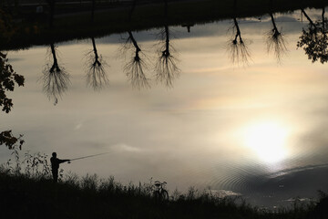 Silhouette of a fisherman at sunset on a calm lake with reflections