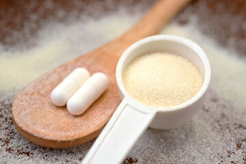 Collagen powder in a plastic measuring spoon and supplement tablets on a wooden spoon. Essential nutritional supplement to promote the health of hair, skin, joints, and nails.