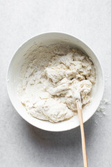 Overhead view of artisan bread dough being mixed in a white bowl, process of making bread dough