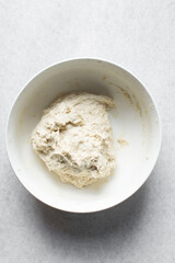 Overhead view of artisan bread dough being mixed in a white bowl, process of making bread dough