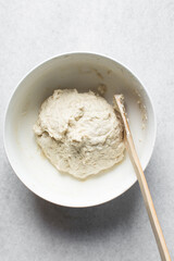 Overhead view of artisan bread dough being mixed in a white bowl, process of making bread dough