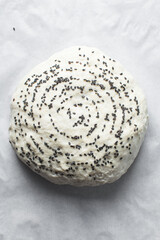 Overhead view of sourdough bread dough with black sesame seeds about to be baked, scored artisan bread dough on parchment lined baking tray, process of making homemade bread