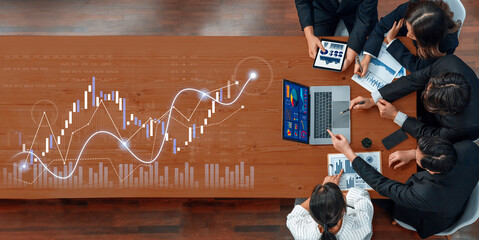 A diverse business team collaborates to analyze financial data on a wooden desk. They utilize technology and charts to strategize for growth and performance. Scalp