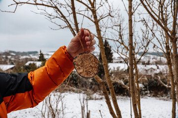 Feeding the birds. A mans hand hangs a bird feeder on a branch in a winter garden © Yuliya