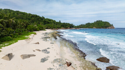 Sandy beach with scattered rocks and lush greenery bordering the shoreline. Anse Bazarca. Seychelles, Mahe.