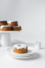 Mini bundt cakes covered in a white glaze on a white countertop, small vanilla bundt cake with a white glaze and tangerine segment on a white background