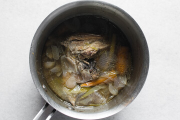 Overhead view of ingredients for making chicken broth in a silver saucepan, top view of raw chicken carrots green chilli spring onions in a saucepan, process of making chicken broth