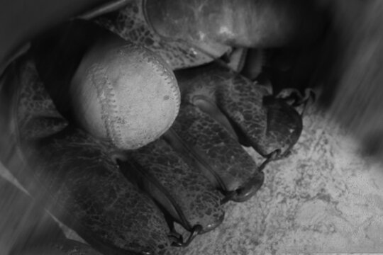 Old grunge baseball background with nostalgic style in black and white showing used ball in vintage glove closeup.