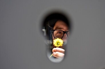 Un joven sostiene una flor amarilla mientras es fotografiado a través del ojo de una cerradura.