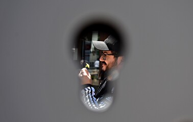 Un joven sostiene una flor amarilla mientras es fotografiado a través del ojo de una cerradura.