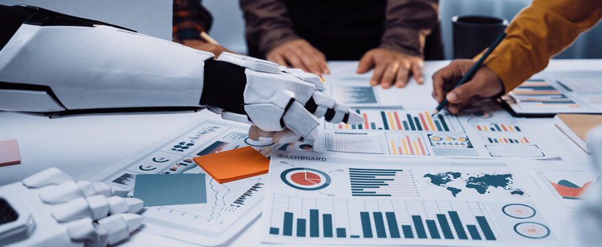 A robotic arm assists professionals in a modern office environment, enhancing teamwork and innovation while analyzing business data and strategies on the workspace table.Noogenesis - Powered by Adobe