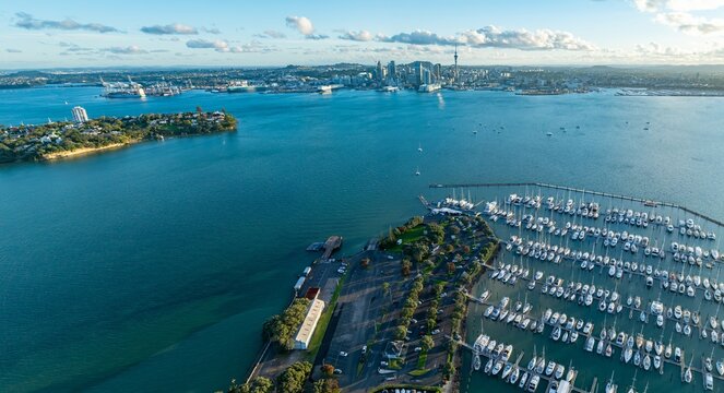 Aerial view of Auckland, New Zealand, showing the harbor, city skyline, and Bayswater marina filled with sailboats. The photo captures the beauty of the coastal city.