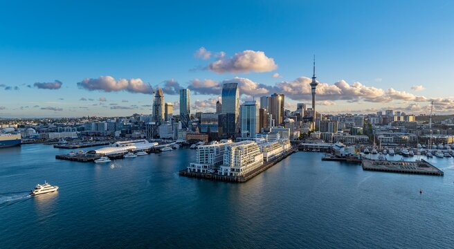 Auckland, New Zealand cityscape at sunset. A boat cruises on the water in the foreground, with the city skyline and Sky Tower in the background. The photo captures the beauty of the city.