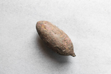 Overhead view of dirty organic sweet potato on a white countertop