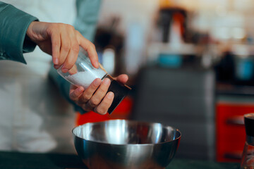 Housewife Ads Salt from a Salt Shaker into a Mixing Bowl. Cheerful event organizer feeling excited about the Xmas corporate festivity

