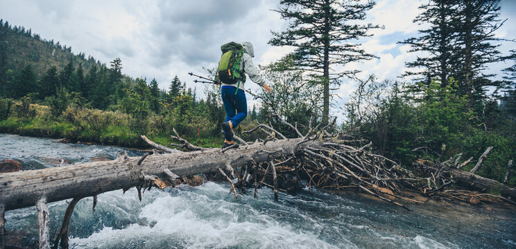 Woman backpacker walking on a one plank bridge in high altitude mountains