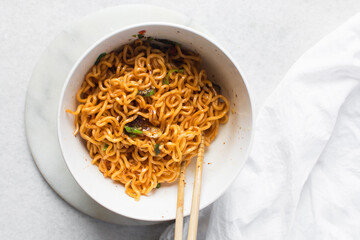 top view of red spicy noodles with sliced peppers in a white bowl