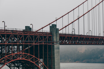 Side view of the Golden Gate Bridge framed by steel beams under an overcast sky.