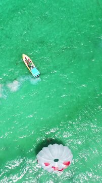 People having fun doing paraseiling in Atlantic ocean with reef and turquoise water, caribbean vacation. Aerial view. Vertical footage