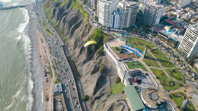 Drone follow shot of a paraglider flying over the Costa Verde in Miraflores, Peru on a summer afternoon.