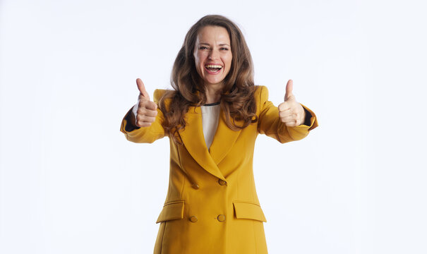 A smiling businesswoman in mustard yellow blazer gives double thumbs-up gesture, radiating positivity and approval. Against plain white background, she embodies confidence, success and agreement - Powered by Adobe
