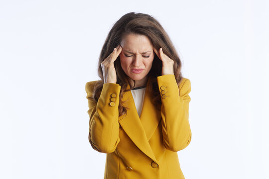 An executive woman in a mustard yellow blazer holds her temples with closed eyes, conveying intense stress, a headache, or professional burnout in a demanding corporate environment.