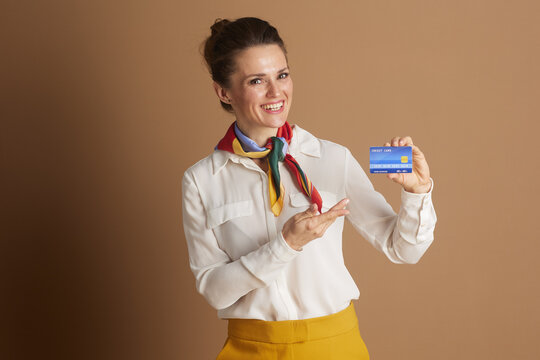A confident, smiling professional woman in a white blouse and colorful scarf highlights a blue credit card, representing modern financial services, purchasing power, and consumer convenience. - Powered by Adobe
