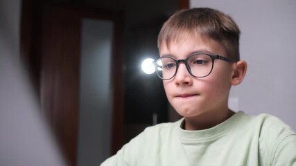 Young boy in black rimmed glasses intently viewing a bright monitor, focused on digital learning and screen based study, illustrating childhood education and modern tech use