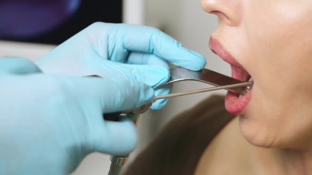 Closeup view of ENT doctor performing throat endoscopy with endoscope tool inside patient mouth in modern clinic for medical examination and diagnostics.