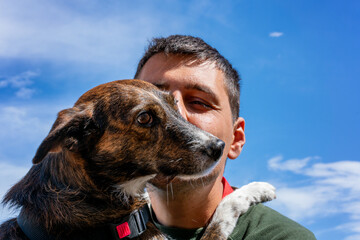 Man holding and embracing a brown dog against a blue sky sharing a moment of companionship
