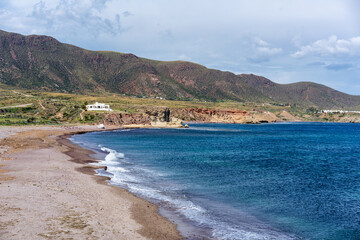Los Escullos beach in Cabo de Gata with waves washing ashore mountains and white houses in the background in Spain