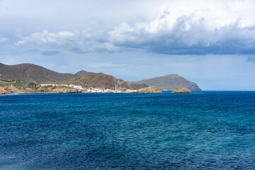 Deep blue sea reflecting cloudy sky, with coastal village nestled among mountains in Los Escullos beach in Cabo de Gata, Spain