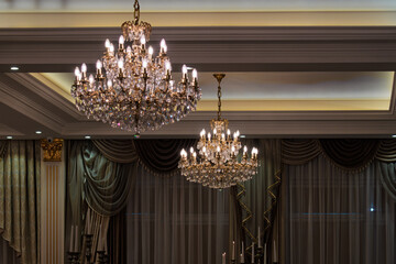 Vilnius, Lithuania - May 9 2025 - Two ornate crystal chandeliers illuminate a dimly lit room with elegant drapes and candelabras, suggesting a formal event or luxurious setting.