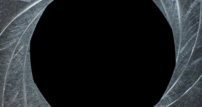 Circular blades of a mechanical iris create a precision opening controlling amount of light entering a camera lens with the opening mechanism controlling the aperture and the depth of field in focus.