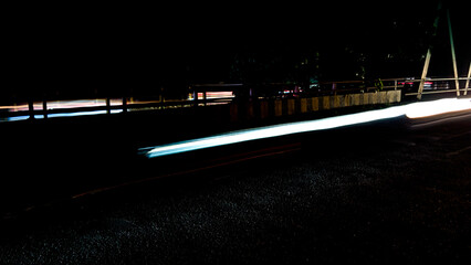 Brightly colored lines of light extend in rapid motion across the dark asphalt, creating a dramatic...
