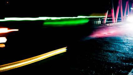 Brightly colored lines of light extend in rapid motion across the dark asphalt, creating a dramatic...